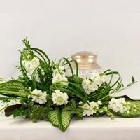 A white and green flower arrangement surrounding a cremation urn.